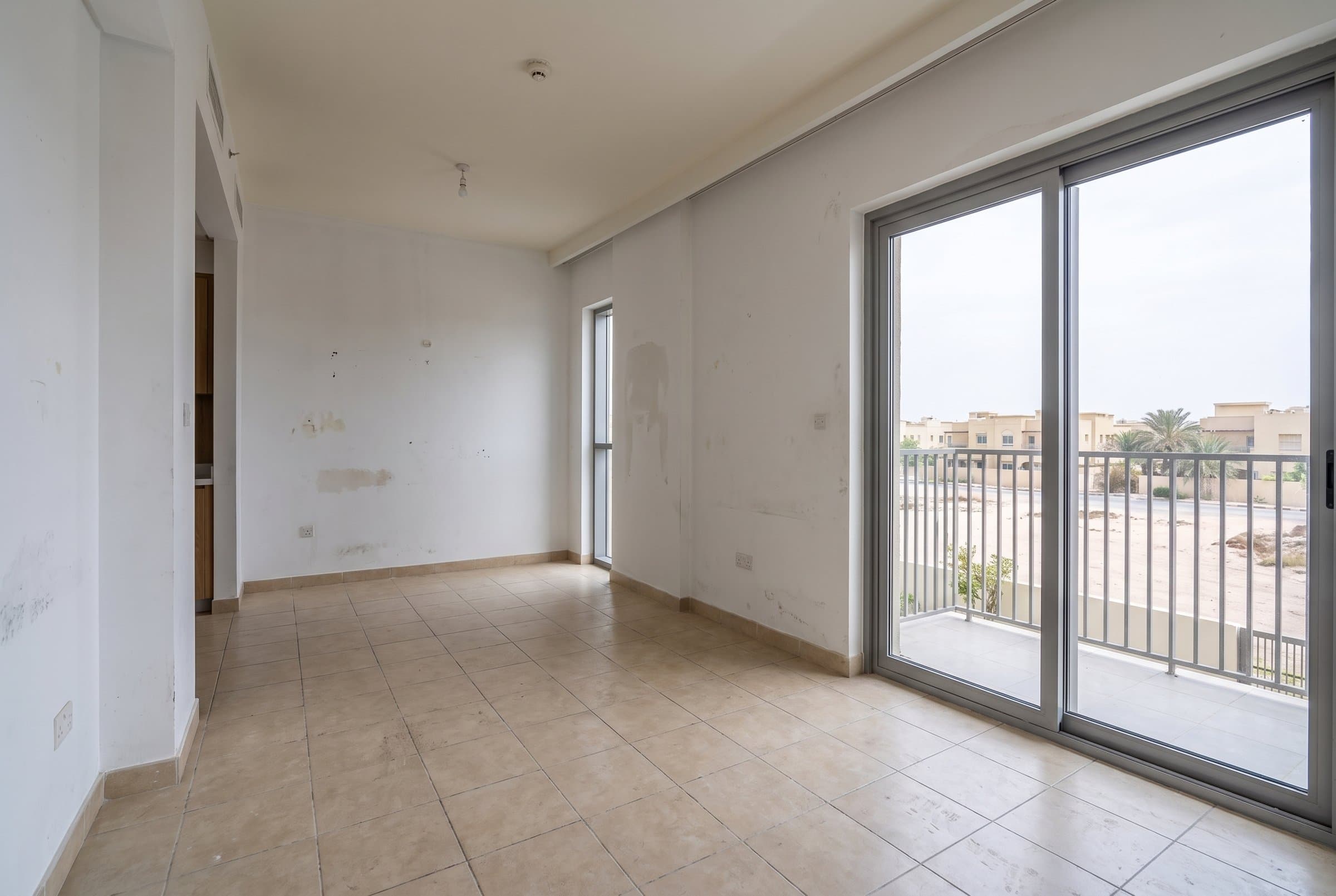 Before: Empty studio apartment before renovation, with a tiled floor, marked walls and a balcony door