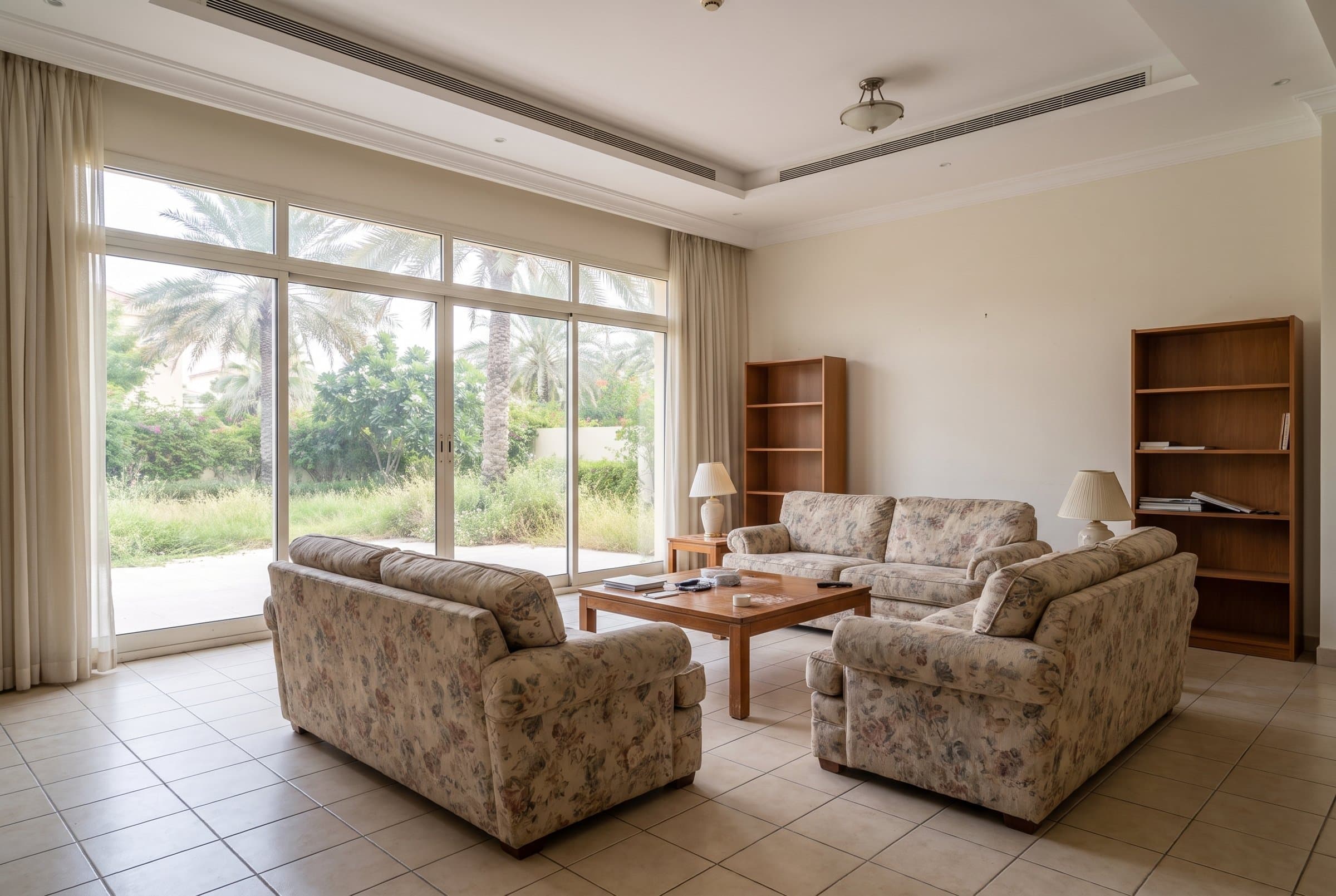 Before: Villa living room before renovation, with floral sofas, tiled floor and sliding glass doors